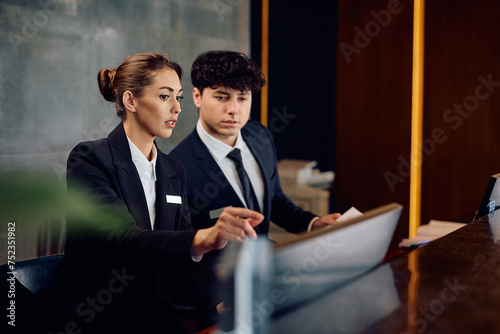 Two receptionists cooperating while working on computer at hotel front desk. photo