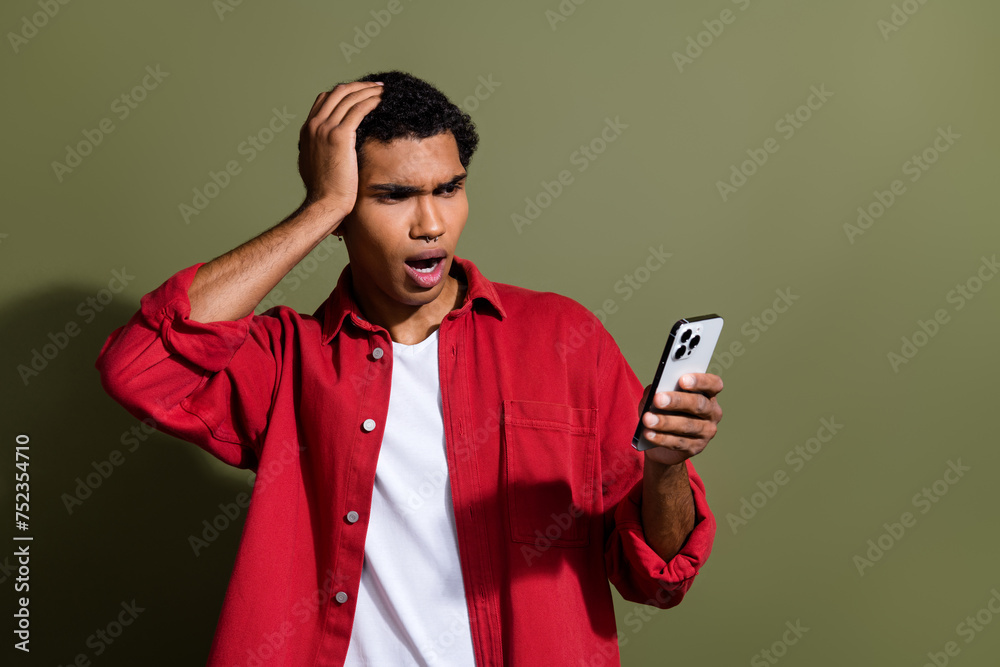 Photo of funky impressed man dressed red shirt getting dislikes modern device empty space isolated green color background Photo of funky impressed man dressed red shirt getting dislikes modern device empty space isolated green color background