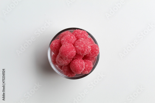Soursop candy, in pink color and ball shaped, coated by sugar. In transparent glass bowl. Isolated on white background, flat lay or top view photo