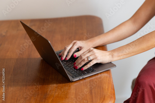 Fototapeta Naklejka Na Ścianę i Meble -  young woman's hands with slender fingers and rings and red nailpolish on laptop on top of wooden table, working from home