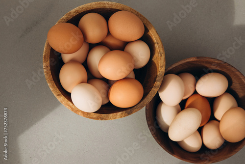 Chicken eggs of different brown and beige shades in a large wooden bowls on a grey background. Easter background. Top view