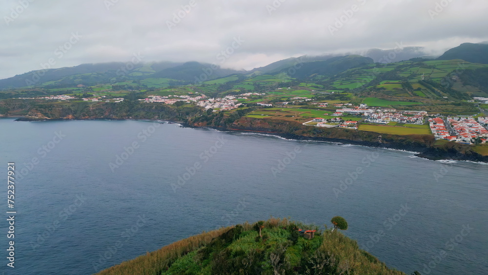 Panoramic cliff coastline town on cloudy day. Drone shot of blue water washing