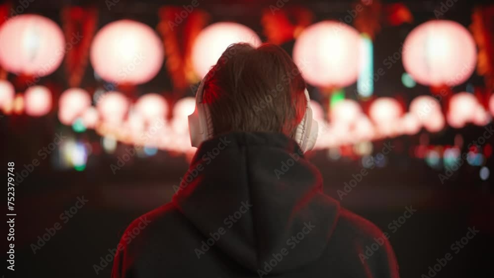 Young man enjoying music in large wireless headphones at night in the city. Back view. Young man enjoying music in large wireless headphones at night in the city. Back view.
