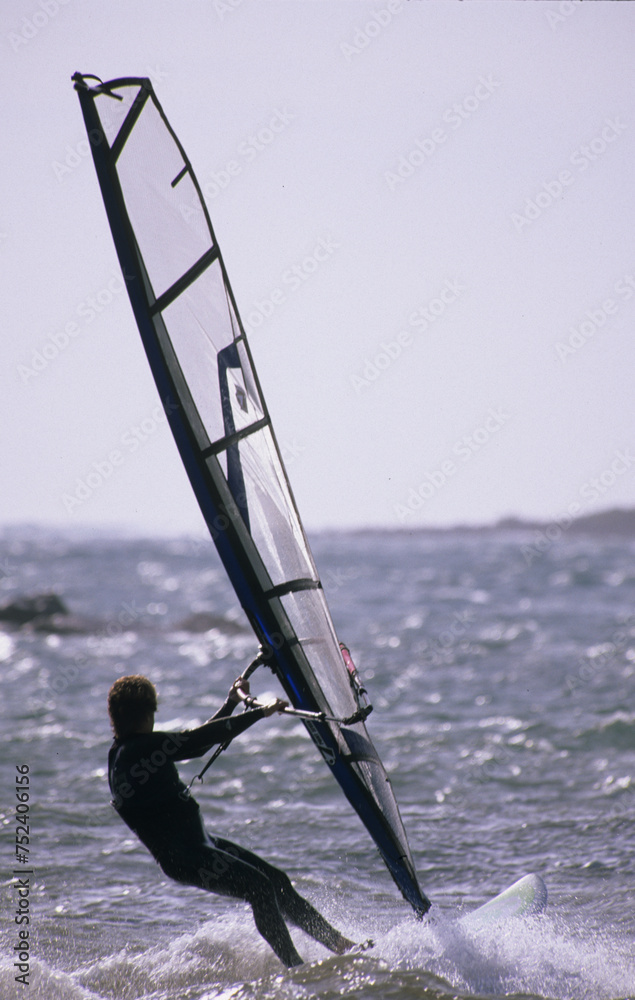 Naklejka premium Panned shot of a windsurfer sailing high speed, unrecognizable person. Alghero, Sardinia, Italy