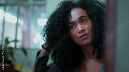 Young African American 20s woman getting ready to go out, plays with curly hair and adjusting hairstyle before leaving, clsoe-up face © Marco