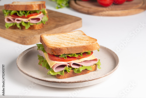 Close-up of two sandwiches with bacon, salami, prosciutto and fresh vegetables on rustic wooden cutting board. Club sandwich concept