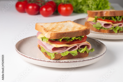 Close-up of two sandwiches with bacon, salami, prosciutto and fresh vegetables on rustic wooden cutting board. Club sandwich concept