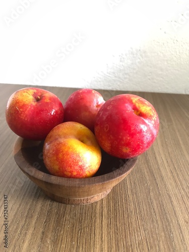 Red plum in bowl on a wooden background with copy space
​ photo