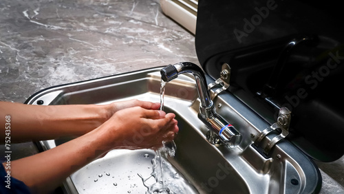 Washing the hands in the sink under the tap with clean water, modern kitchen interior style of the motorhome.