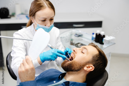 A handsome man is sitting in a chair at a woman's appointment at the dentist's office