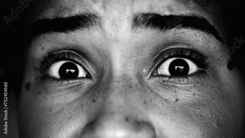 Macro close-up of a scared person looking directly at camera in worry and anxiety, intense dramatic monochromatic facial detail of boggled wide eyes being afraid