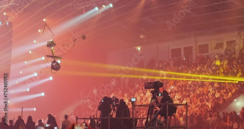 Professional filming of musical performance at live concert light. Videographers group film on platform, entertainment show event in spotlights equipment. Television broadcast, backstage production photo
