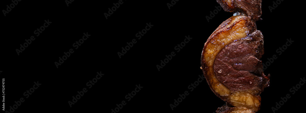 Picanha. Brazilian traditional steak in barbecue. Slices of grilled Picanha on a spit with the black background in Brazil.