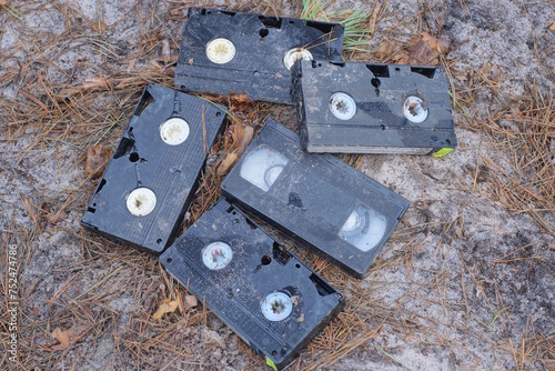a pile of five black plastic dirty old video cassettes lie on the gray ground on the street