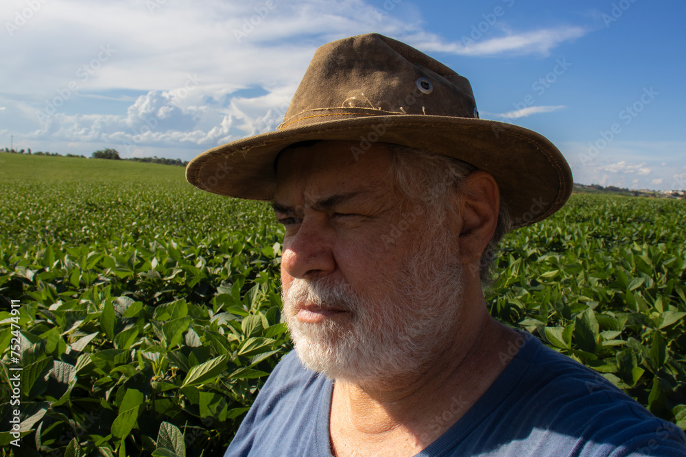 Middle-aged Brazilian farmer, between 50 and 60 years old, observes a soybean plantation on a sunny day in rural Brazil