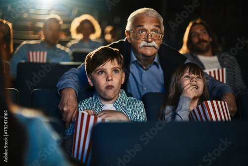 Grandfather and grandchildren watching film in movie theater photo