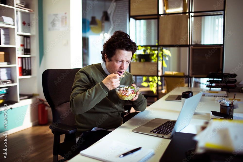 Young businessman eating a salad in the modern office