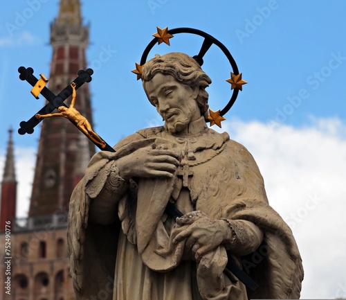 The statue of Saint John of Nepomuk, adorned in intricate detail and solemn expression, stands as a revered symbol of faith and devotion, casting a watchful gaze over the faithful below.     