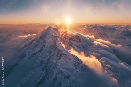 Aerial view of snow covered mountains with the sun rising above the clouds.