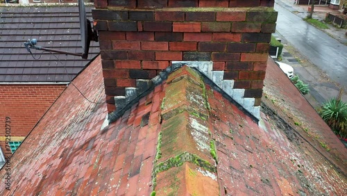 Aerial footage of a typical British house showing a close up shot of the roof and chimney with the tiles needed cleaning on top of the roof on a rainy wet day in the UK photo