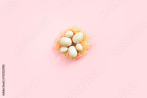 Wooden eggs lying on artificial nest in the center on pink background. Easter eco-friendly concept