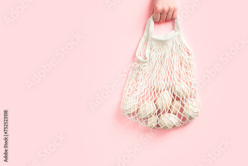 Eco-friendly concept with wooden eggs in cotton bag on pink background. Easter holiday