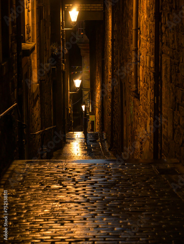 A dark and narrow alley in a picturesque medieval town lit by street lanterns