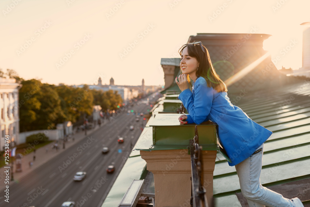 Young happy woman in jeans and blue jacket resting on rooftop in St Petersburg