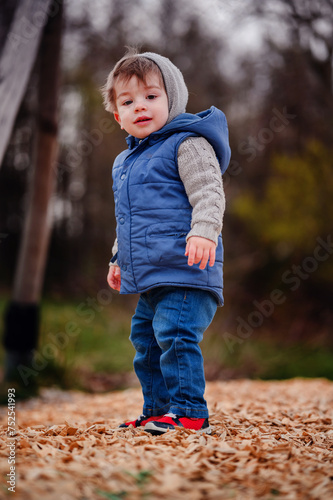 Photography A young boy, full of life, stands in a playground covered with wood chips, the c