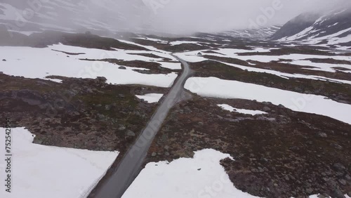 aerial view of a mountain road along a frozen Norwegian river and lake in a valley between mountains with snow on a cloudy day. 4k.