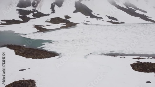 aerial view of a frozen norwegian river and lake between snowy mountains on a cloudy day. 4k.