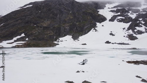 aerial view of a frozen norwegian river and lake between snowy mountains on a cloudy day. 4k.