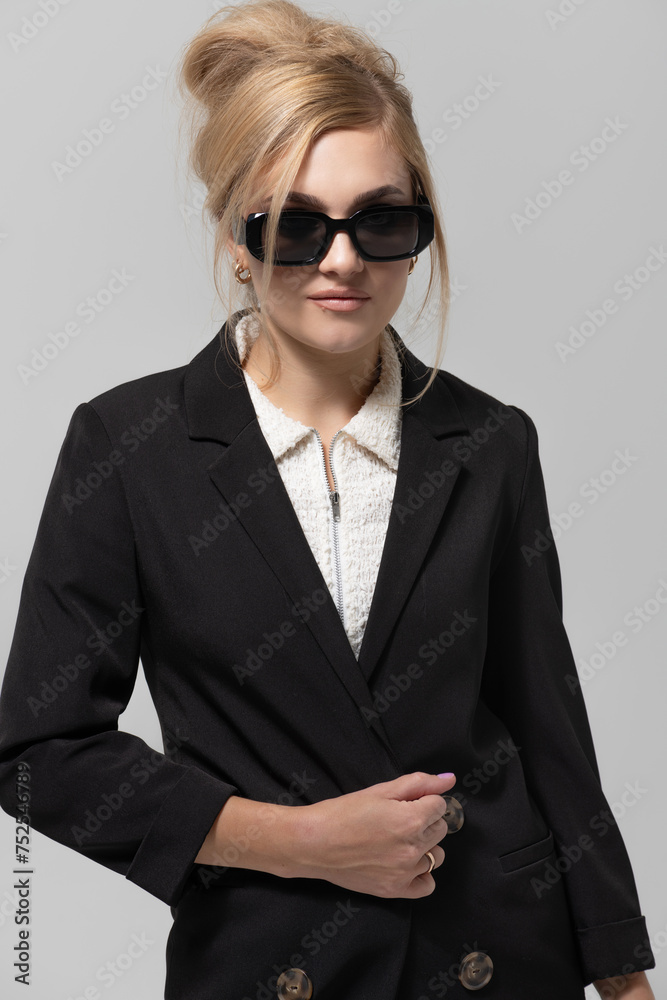 Beauty, fashion, make-up and hairstyle concept. Beautiful young blonde woman wearing black suit and sunglasses studio portrait. Girl with fancy hairstyle. Model holding one hand near belly Beauty, fashion, make-up and hairstyle concept. Beautiful young blonde woman wearing black suit and sunglasses studio portrait. Girl with fancy hairstyle. Model holding one hand near belly