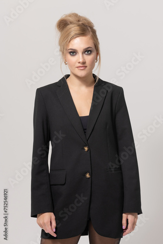 Beauty, fashion, make-up and hairstyle concept. Beautiful young blonde woman wearing black suit studio portrait. Girl with fancy hairstyle. Model standing still and looking at camera