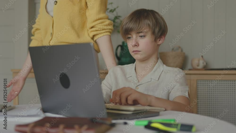 Unhappy teenager child boy doing homework in apartment while young mother shouting screaming teaching negatively at him. Negative emotions and domestic education concept. Upset male adolescent Unhappy teenager child boy doing homework in apartment while young mother shouting screaming teaching negatively at him. Negative emotions and domestic education concept. Upset male adolescent