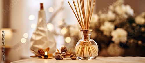 A clear glass vase filled with reeds is placed next to a burning candle, emitting a cozy and aromatic atmosphere. The reeds diffuse scents while the candle adds warmth and ambiance to the space.