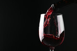 Pouring red wine into glass against black background, closeup. Space for text
