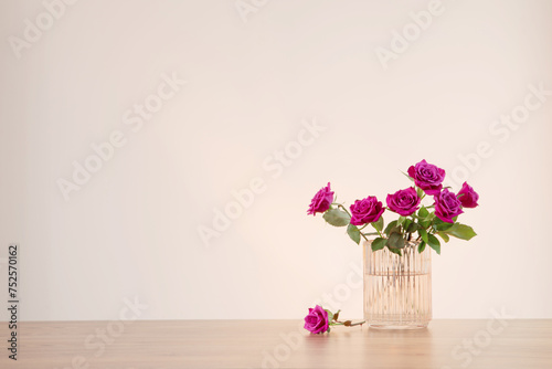 purple roses in glass vase on wooden table 