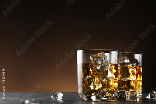 Whiskey and ice cubes in glasses on black table, closeup. Space for text