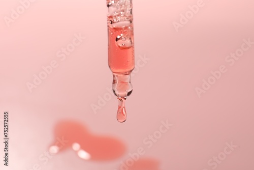 Dripping moisturizing serum from pipette on pink background, closeup © New Africa