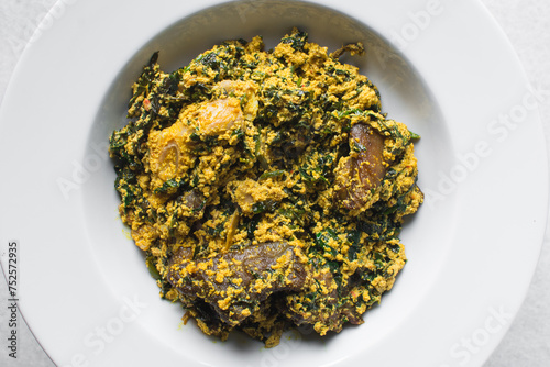 Nigerian egusi soup with fish and beef in a white plate, egusi vegetable soup in a large dinner plate, traditional egusi soup in a white dish photo