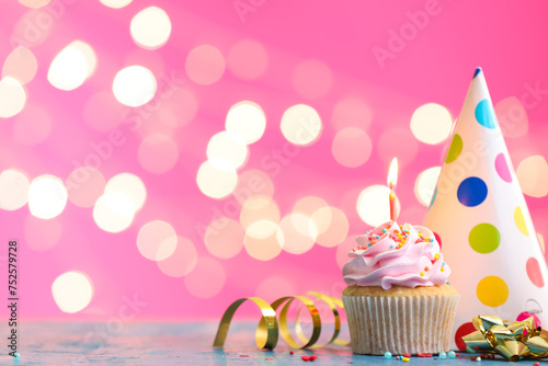 Tasty Birthday cupcake with burning candle and party hat on table against blurred lights