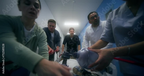 Medical staff and relatives of the victim are running down the hospital corridor carrying the patient on a gurney, giving him oxygen through a mask
