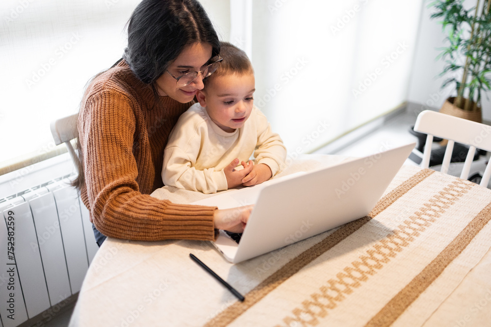 A heartwarming moment as a positive mother embraces her son while they both engage with content on a laptop at home A heartwarming moment as a positive mother embraces her son while they both engage with content on a laptop at home