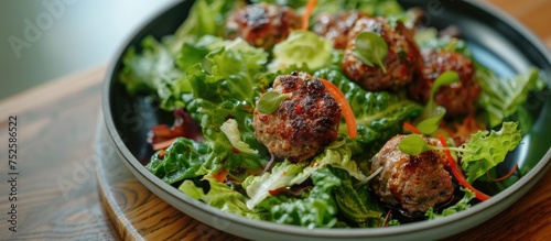 A bowl sits on a table filled with a colorful salad consisting of lettuce, green vegetables, and meatballs. The meatballs are mixed with veggies, creating a delicious and nutritious meal.