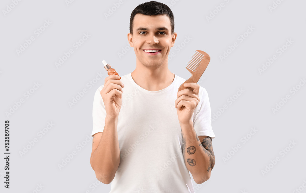 Young man with serum for hair growth and comb on light background Young man with serum for hair growth and comb on light background