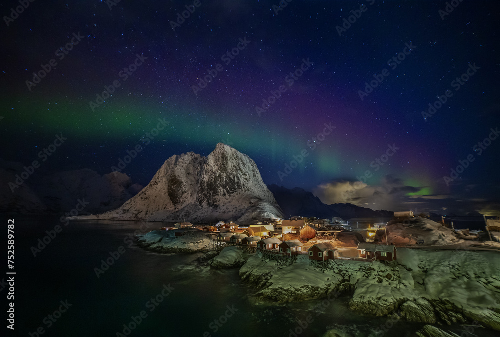 Aurora borealis over the fishing village with traditional red cabins in Hamnoy, Lofoten, Norway