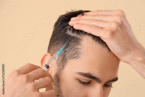 Young man giving himself injection for hair growth on beige background, closeup