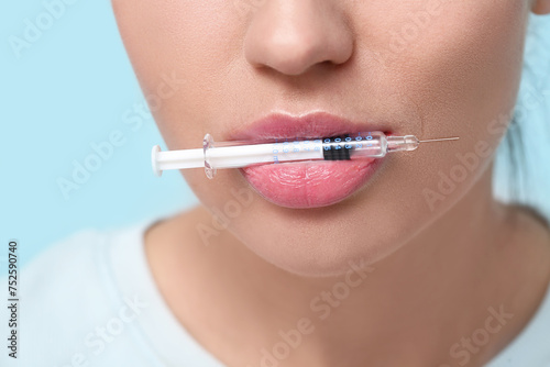 Young woman holding injection syringe in mouth on color background  closeup