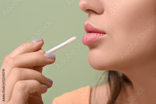 Young woman applying lipgloss on green background  closeup